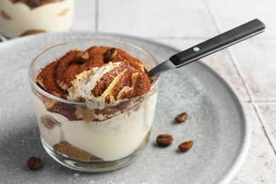 Delicious tiramisu in glass, coffee beans and spoon on light tiled table, closeup