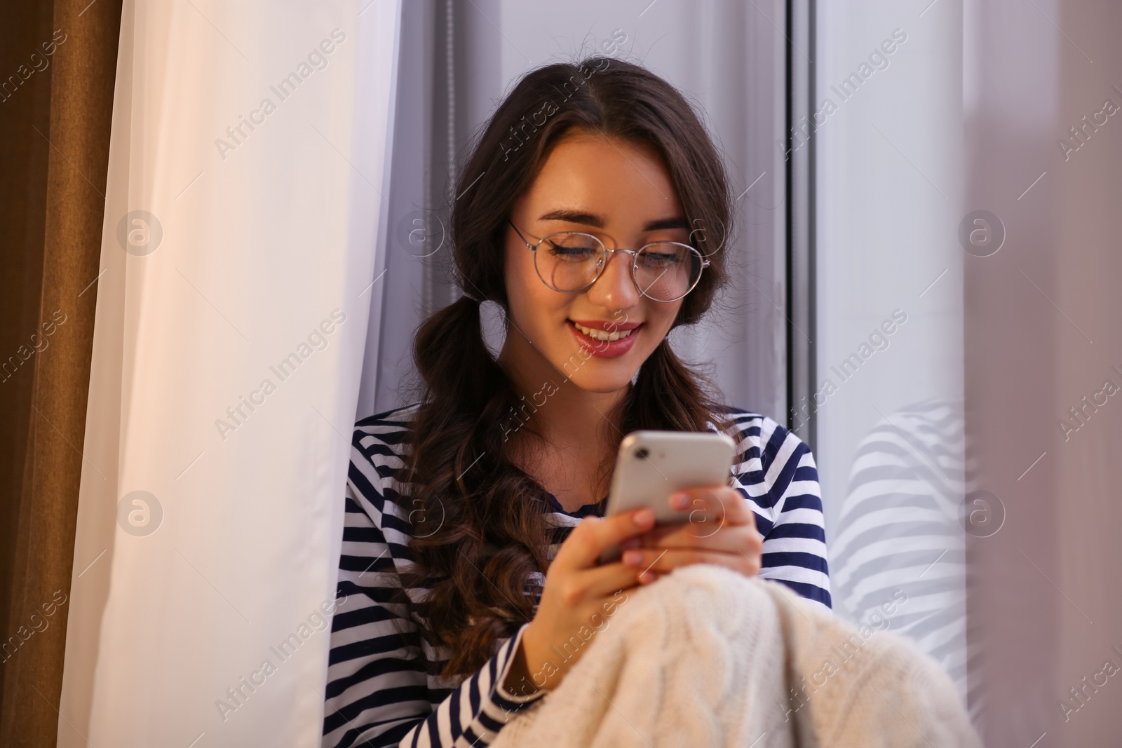 Photo of Young woman using smartphone near window at home. Winter atmosphere