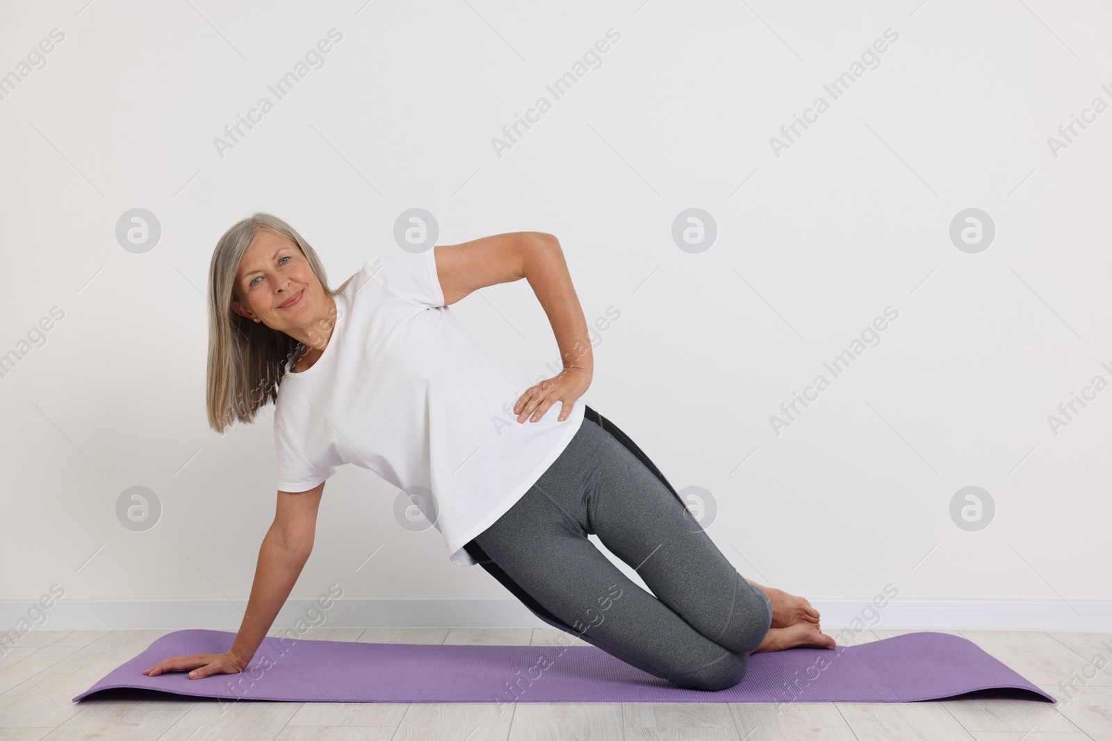 Photo of Happy senior woman practicing yoga on mat near white wall