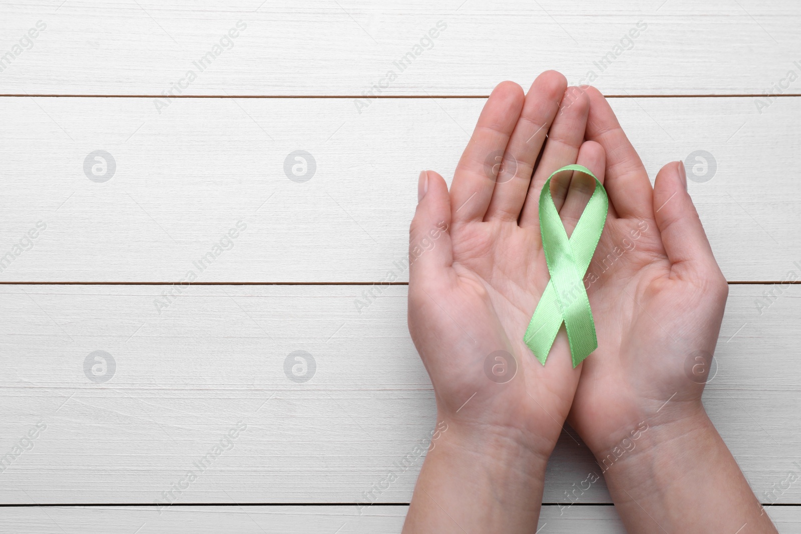 Photo of World Mental Health Day. Woman holding green ribbon on white wooden background, top view with space for text