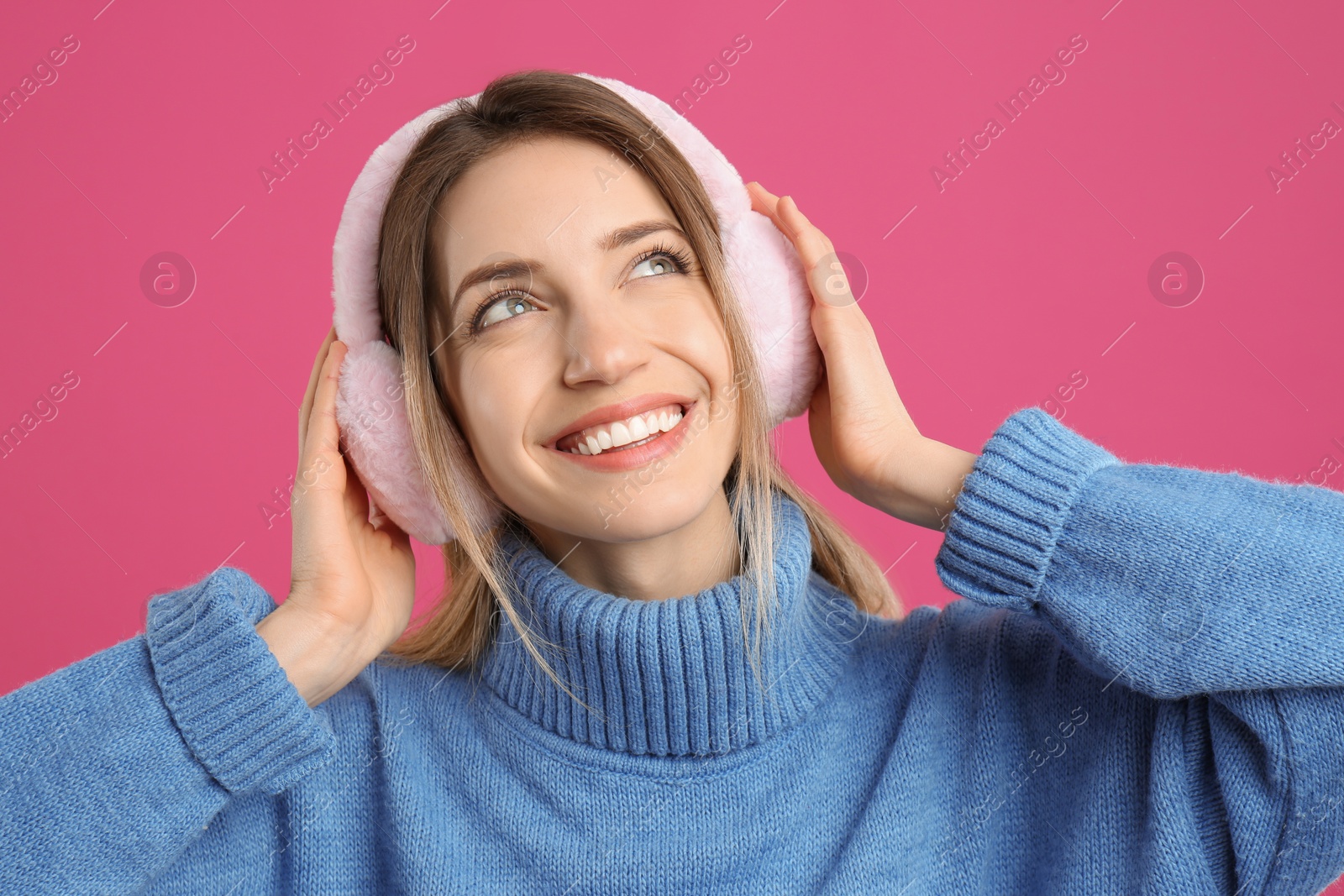 Photo of Happy woman wearing warm earmuffs on pink background