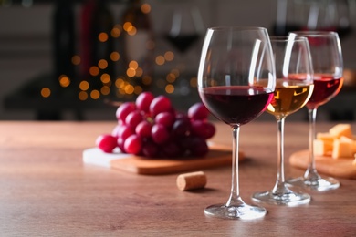 Glasses with different wines and appetizers on wooden table against blurred background. Space for text