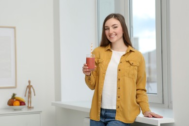 Photo of Beautiful young woman with delicious smoothie near window indoors. Space for text