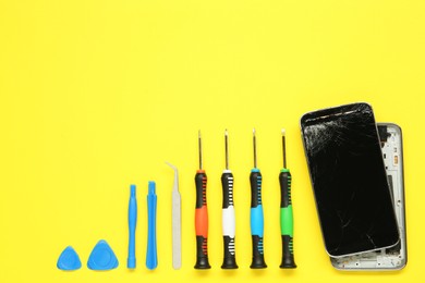 Damaged smartphone and repair tool set on yellow background, flat lay. Space for text