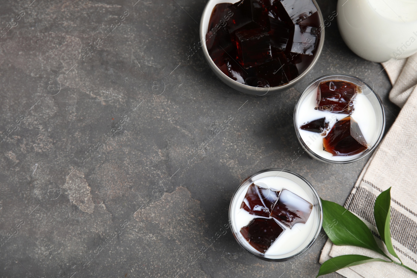 Photo of Glasses of milk with delicious grass jelly on grey table, flat lay. Space for text