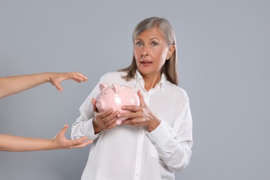 Photo of Scammer taking piggy bank from woman on light grey background. Be careful - fraud