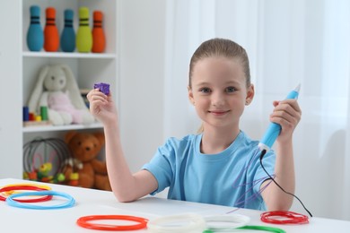 Photo of Girl drawing with stylish 3D pen at white table indoors