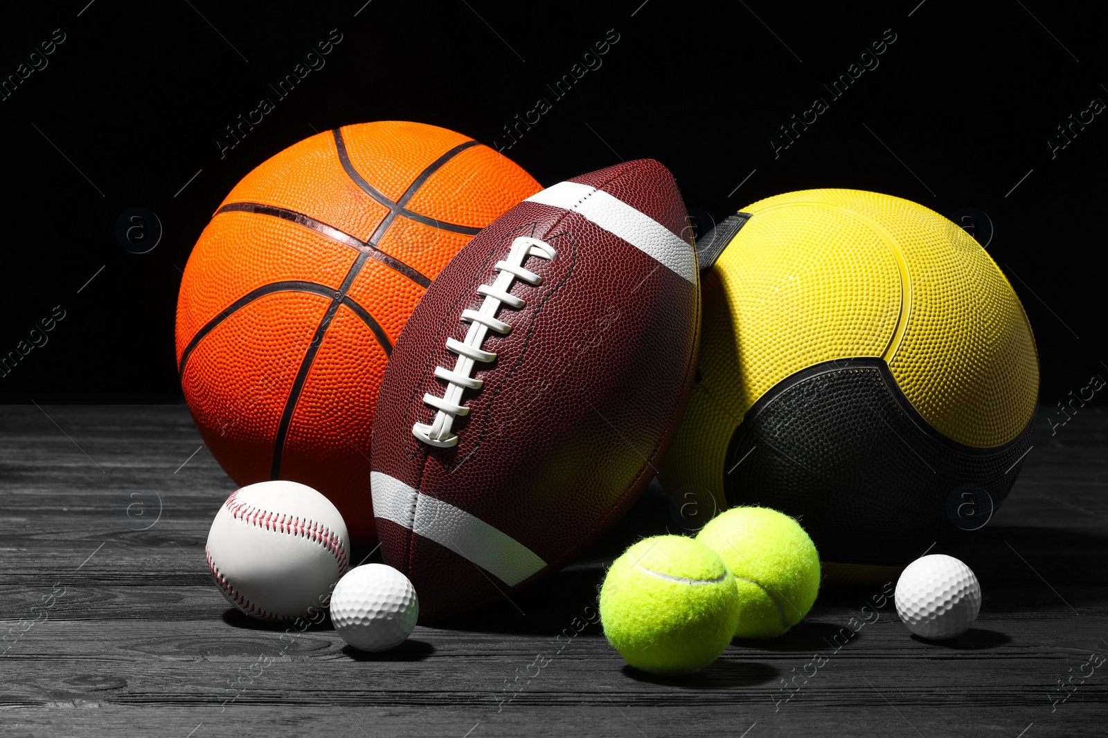 Photo of Many different sport balls on dark wooden table against black background