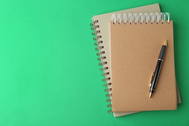 Photo of Notebooks and pen on green background, top view. Space for text