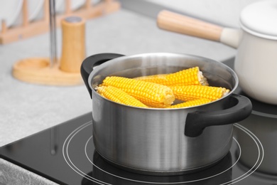 Stewpot with water and corn cobs on stove in kitchen