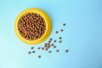 Dry pet food in feeding bowl on light blue background, flat lay. Space for text