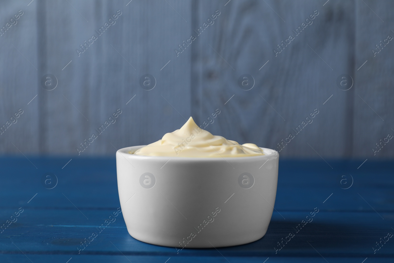 Photo of Tasty mayonnaise in bowl on blue wooden table, closeup. Space for text