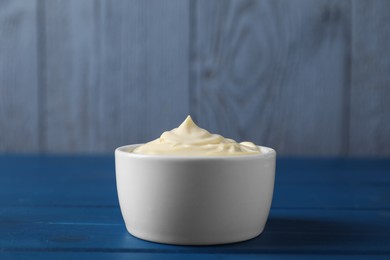 Photo of Tasty mayonnaise in bowl on blue wooden table, closeup. Space for text