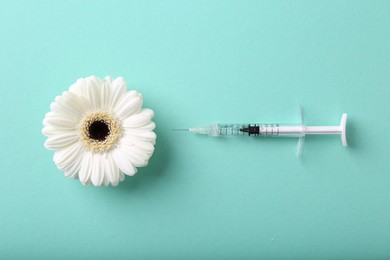 Photo of Cosmetology. Medical syringe and gerbera flower on turquoise background, flat lay