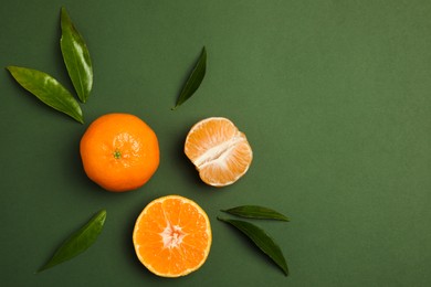 Delicious tangerines and leaves on green background, flat lay. Space for text