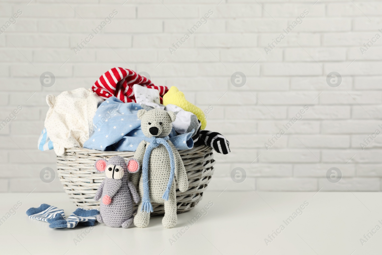 Photo of Wicker basket with laundry and toys on table near white brick wall. Space for text