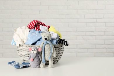 Photo of Wicker basket with laundry and toys on table near white brick wall. Space for text