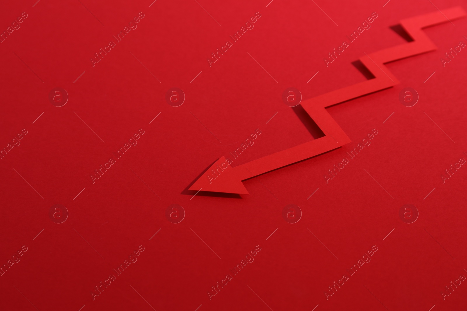 Photo of One zigzag paper arrow on red background, closeup. Space for text