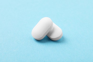 Photo of Two white pills on light blue background, closeup