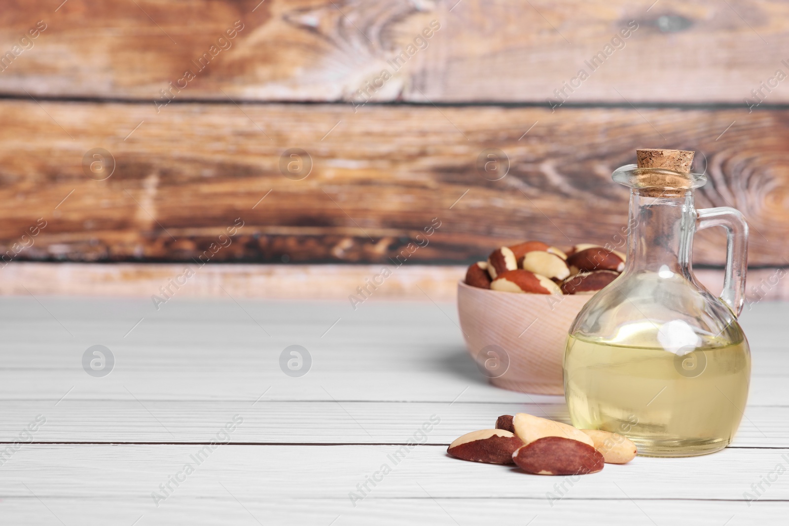 Photo of Tasty Brazil nuts and bottle with oil on white wooden table. Space for text