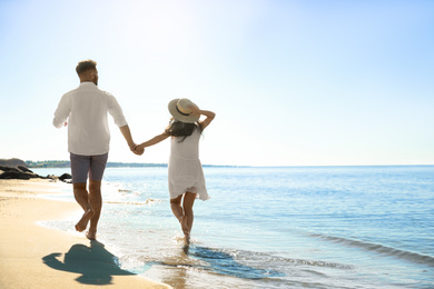 Photo of Young couple running on beach near sea. Honeymoon trip