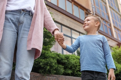 Photo of Happy cute child holding hands with his mother outdoors, low angle view. Family time