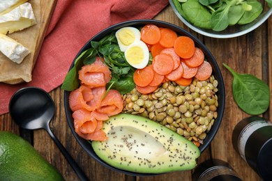 Photo of Delicious lentil bowl with carrot, avocado, egg and salmon on wooden table, flat lay