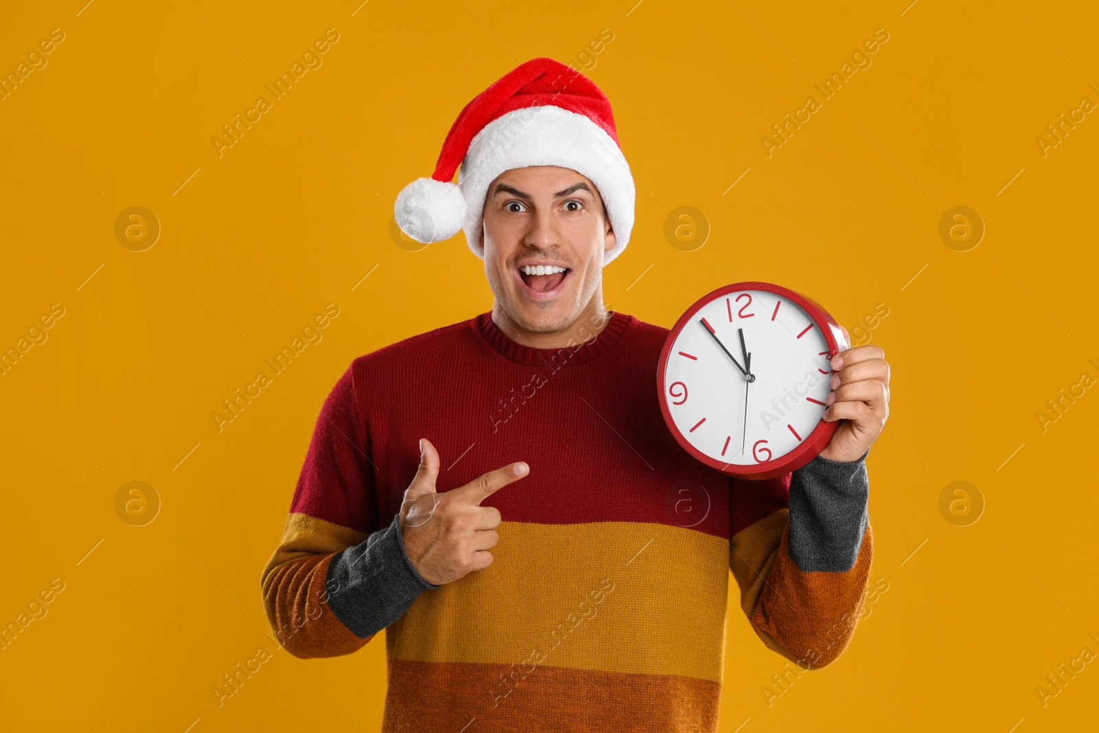 Photo of Man in Santa hat with clock on yellow background. New Year countdown