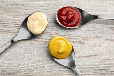 Photo of Spoons with mustard, ketchup and mayonnaise on wooden table, flat lay