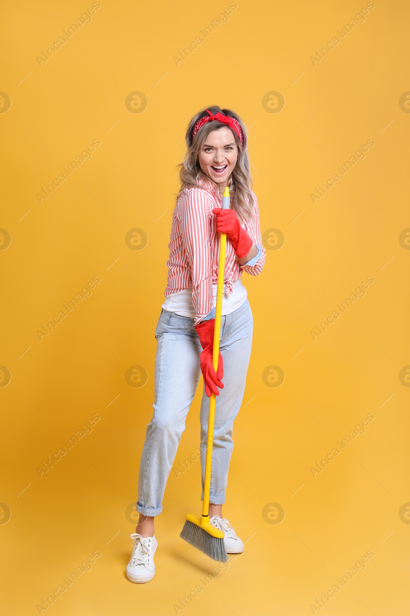 Photo of Beautiful young woman with floor brush singing on orange background