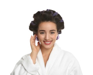 Happy young woman in bathrobe with hair curlers on white background