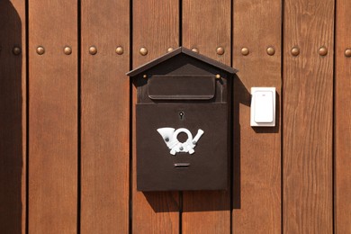 Metal letter box and white doorbell on wooden fence outdoors