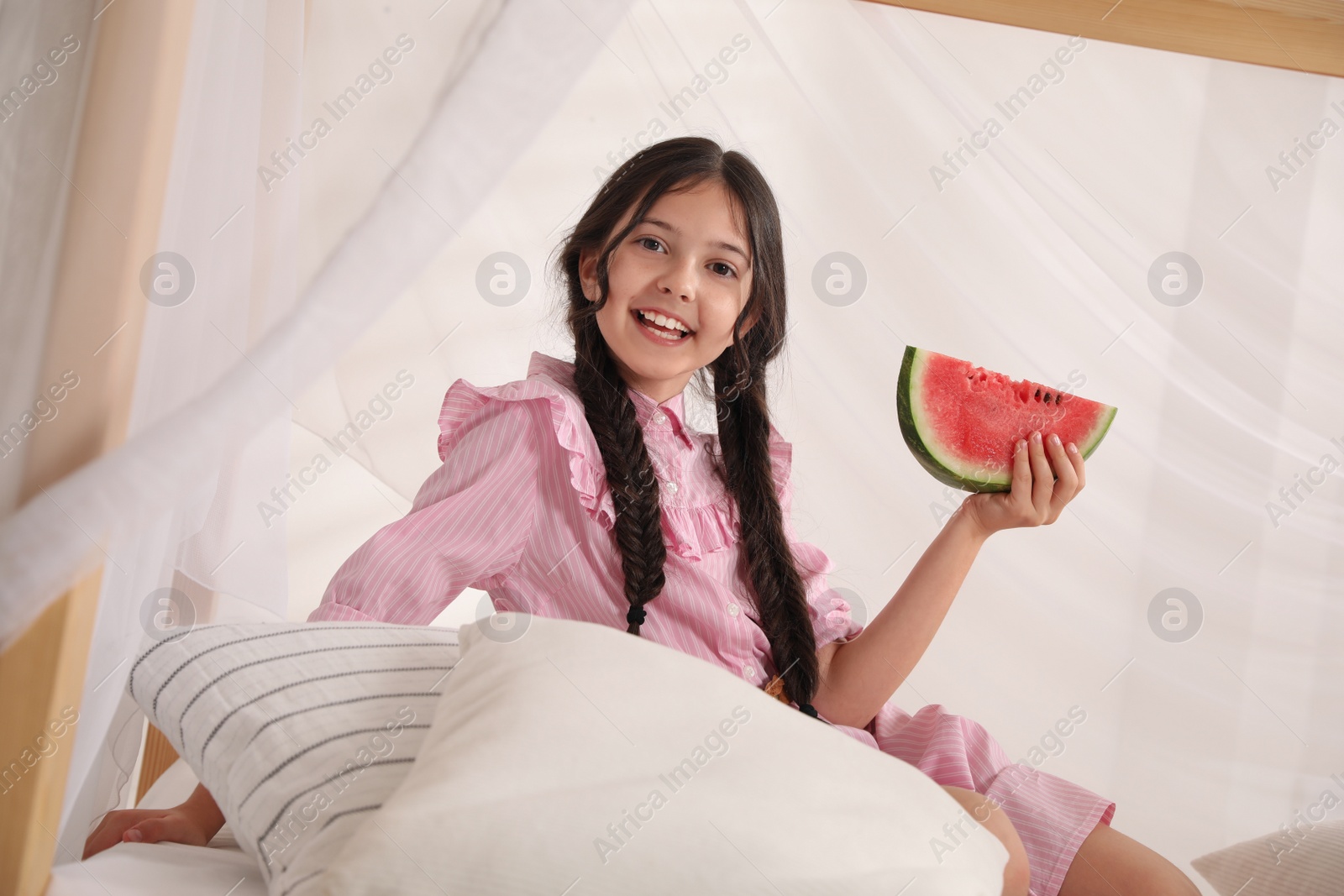 Photo of Cute little girl with watermelon on bed at home