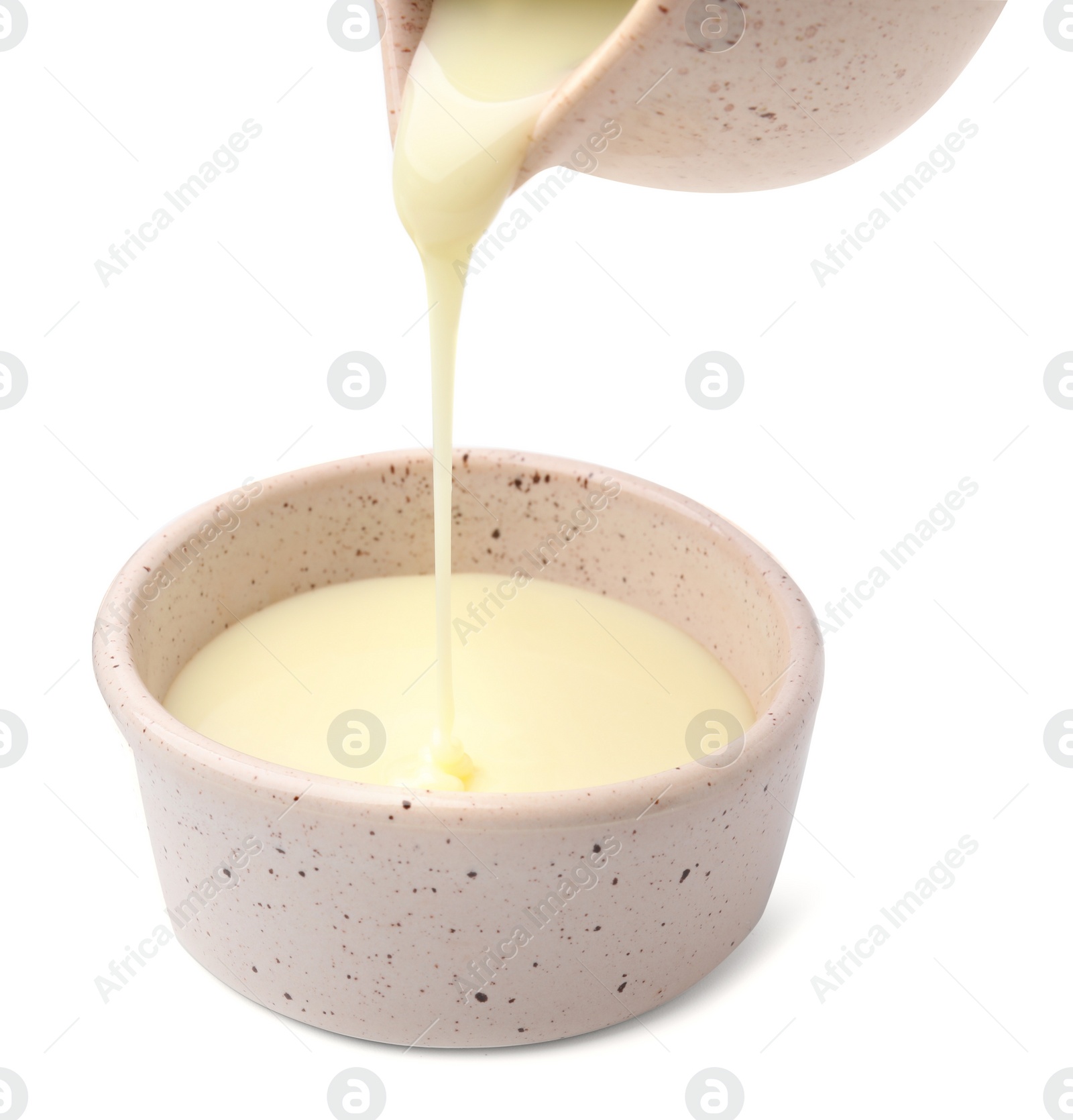 Photo of Pouring condensed milk from jug into bowl isolated on white