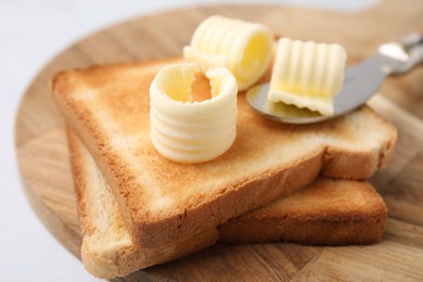 Photo of Tasty butter curls, knife and toasts on white table, closeup