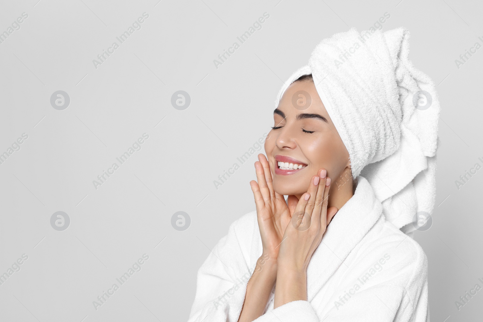 Photo of Young woman in bathrobe with towel on light grey background, space for text. Spa treatment