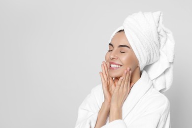 Photo of Young woman in bathrobe with towel on light grey background, space for text. Spa treatment