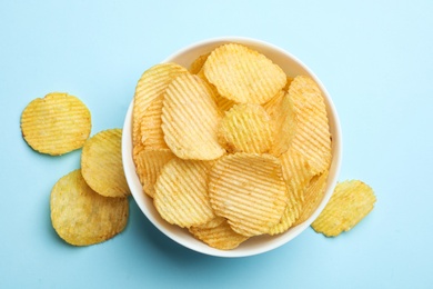 Photo of Delicious crispy potato chips in bowl on color background, top view