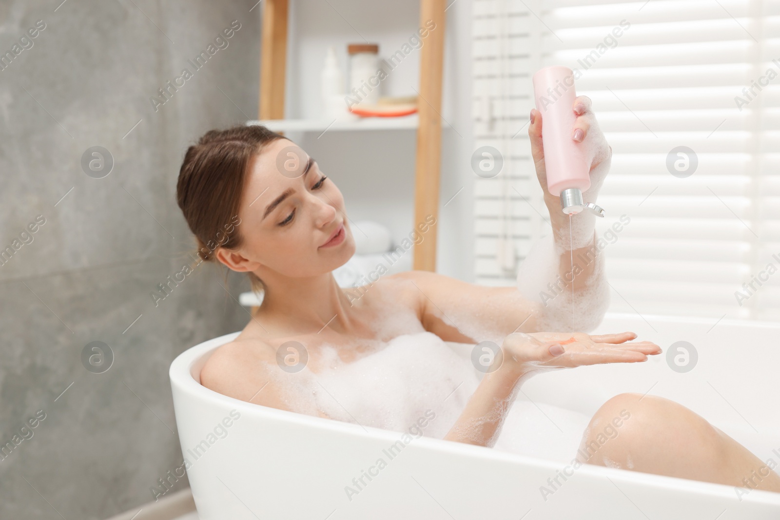 Photo of Woman pouring shower gel onto hand in bath indoors