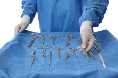 Photo of Doctor holding scalpel near table with different surgical instruments on light background, closeup