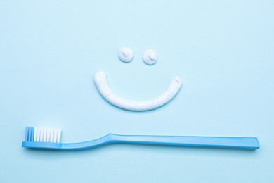 Photo of Funny face made with toothpaste and brush on light blue background, flat lay