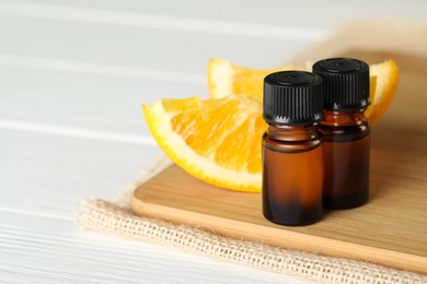 Bottles of essential oil and orange slices on white wooden table, closeup. Space for text