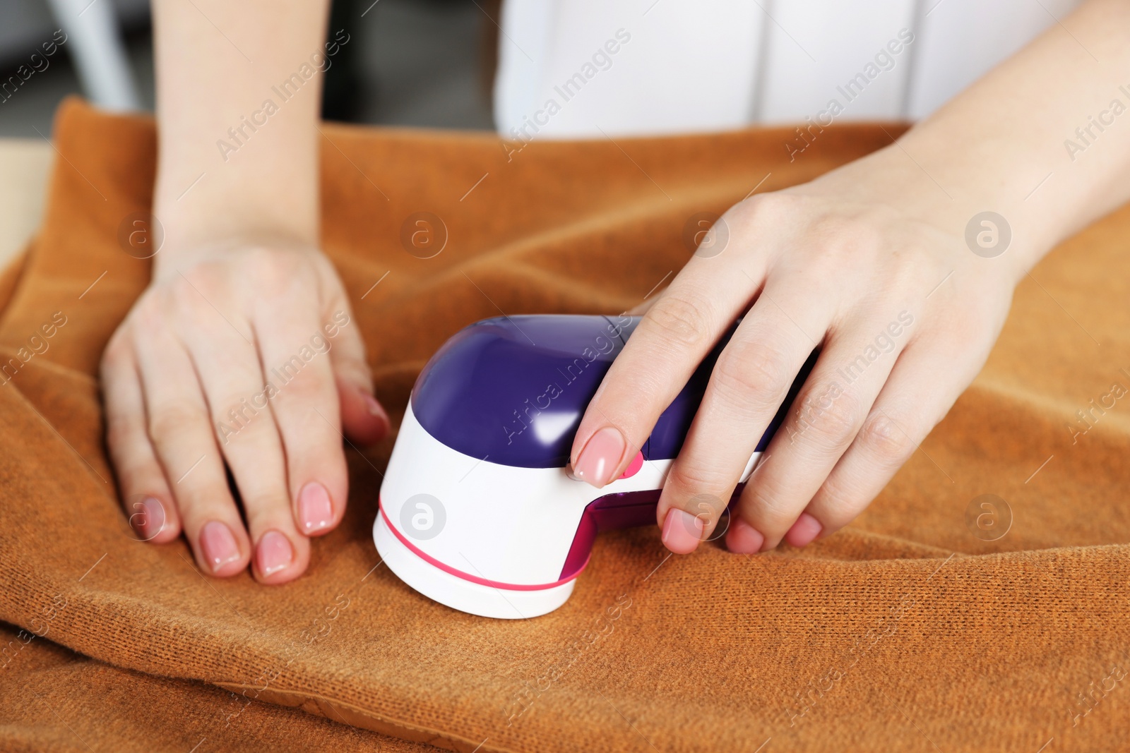 Photo of Woman cleaning clothes with fabric shaver indoors, closeup