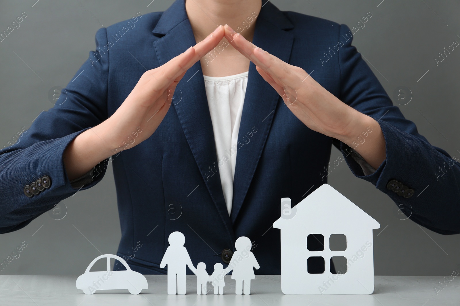 Photo of Woman covering cutout paper family, house and car at table, closeup. Life insurance concept