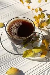 Cup of hot drink and leaves on white wooden table. Cozy autumn atmosphere
