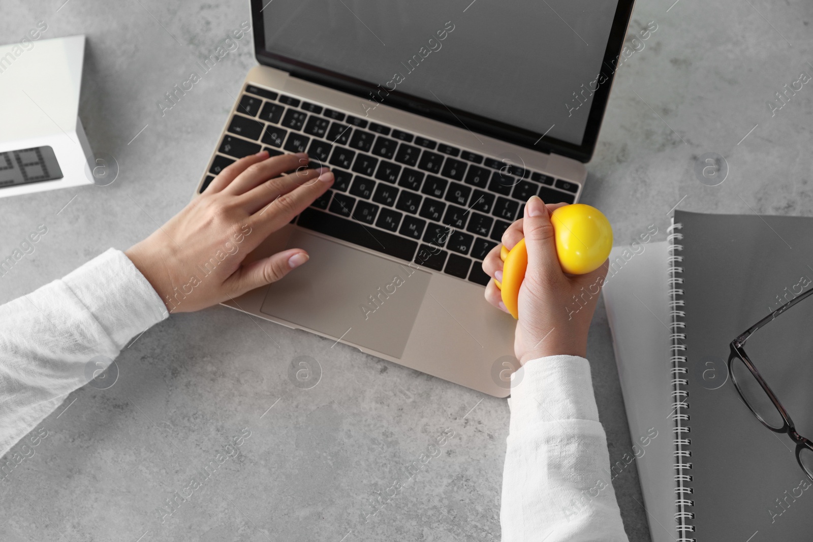 Photo of Woman squeezing antistress ball while working on laptop at table, above view