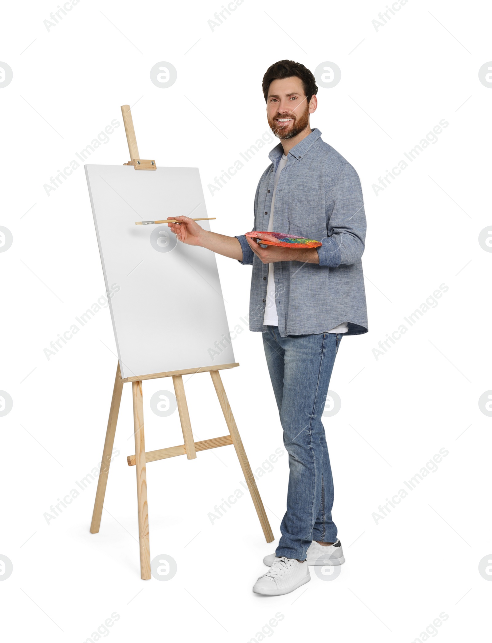 Photo of Happy man with brush painting against white background. Using easel to hold canvas