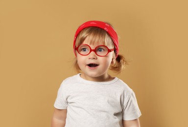 Photo of Cute little girl in glasses on pale brown background