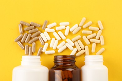 Bottles and different vitamin capsules on yellow background, flat lay