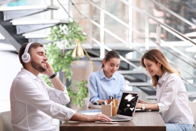 Young businessman with headphones, laptop and his colleagues at table in office